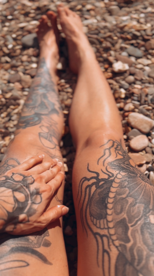 Tattooed legs on a pebbly beach